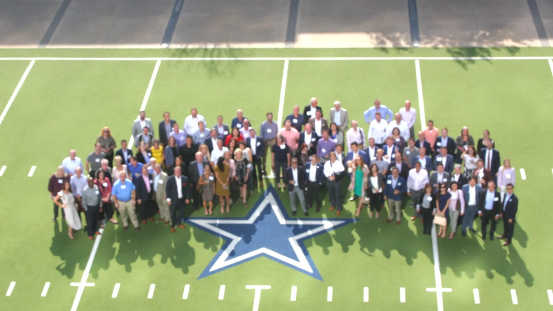 Large group of people standing on a football field around a blue star logo at center field.
