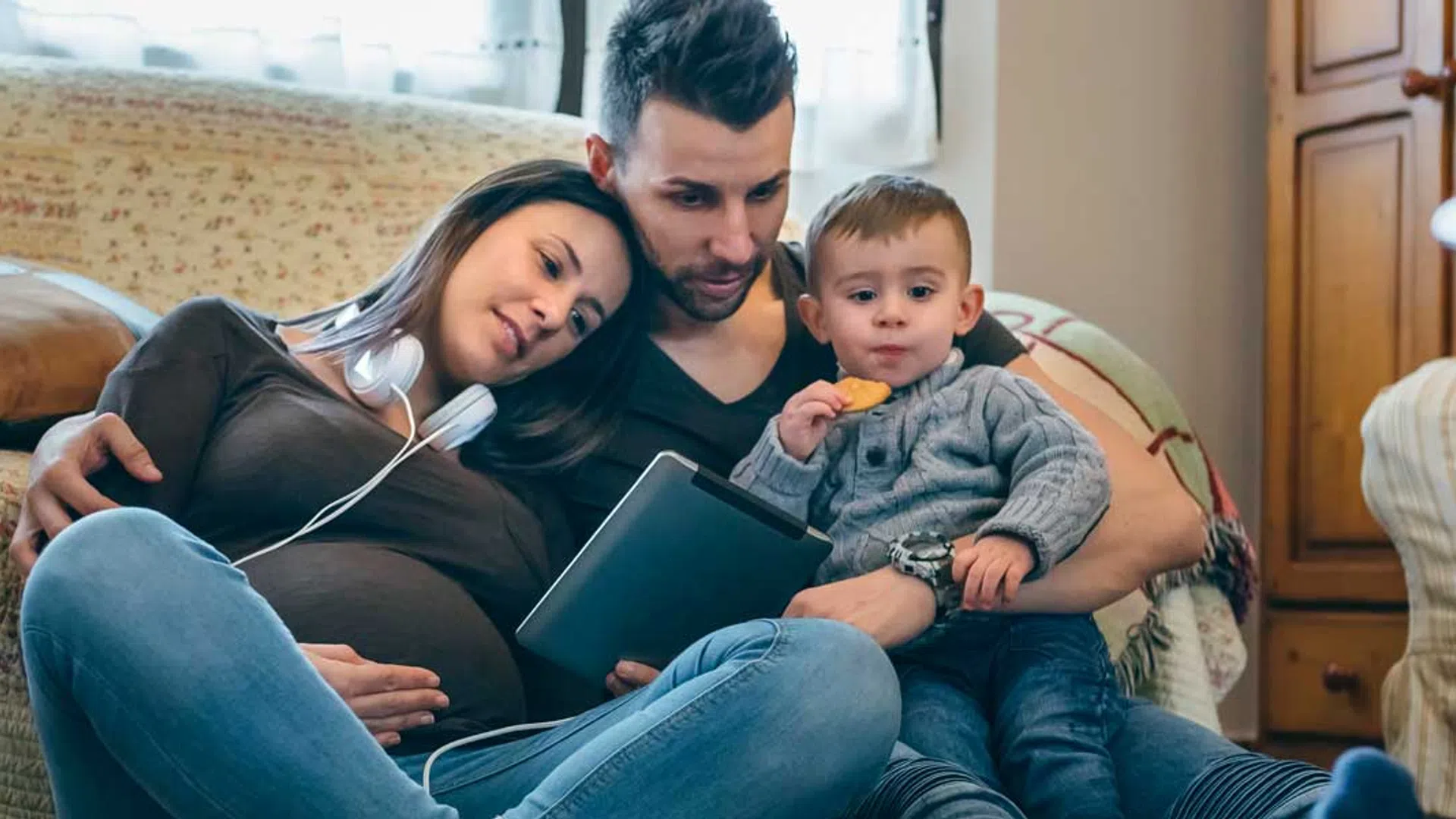 Young family relaxing on couch with tablet, listening to music and spending quality time together at home