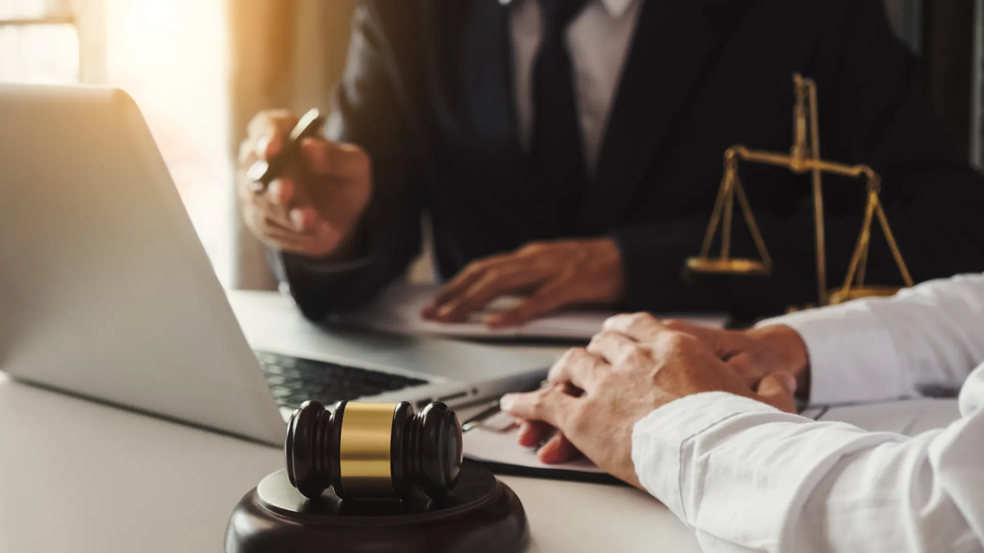 Lawyer and client consulting in office with gavel and scales of justice on desk near laptop