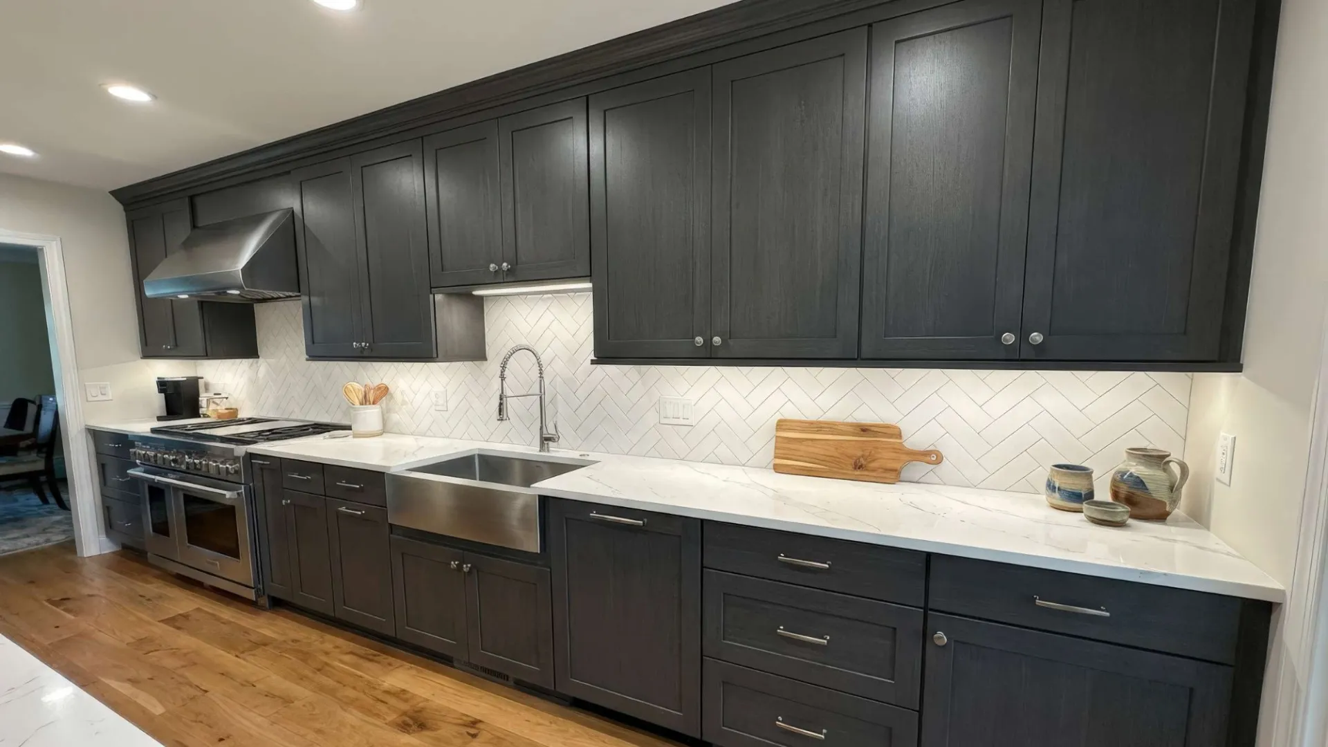 Modern kitchen with dark gray cabinets, white marble countertop, farmhouse sink, and stainless steel appliances.