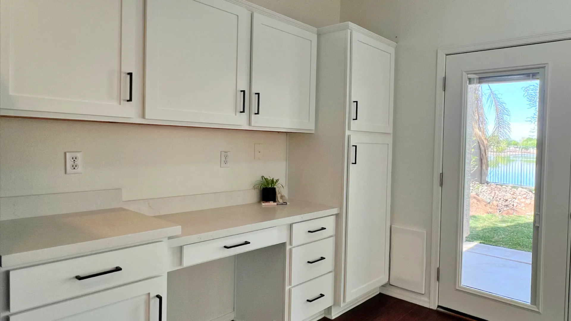 Bright room with white cabinetry, dark wood flooring, and a glass door leading to a sunny outdoor space.