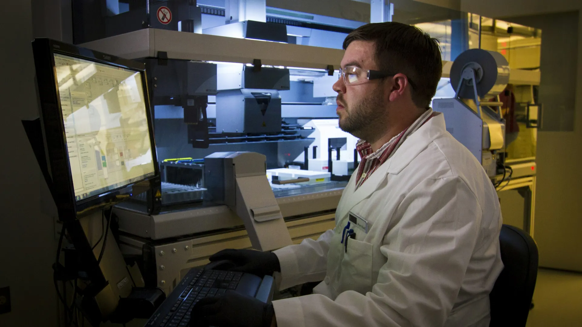 Scientist in a lab coat using a computer with advanced laboratory equipment in a research setting