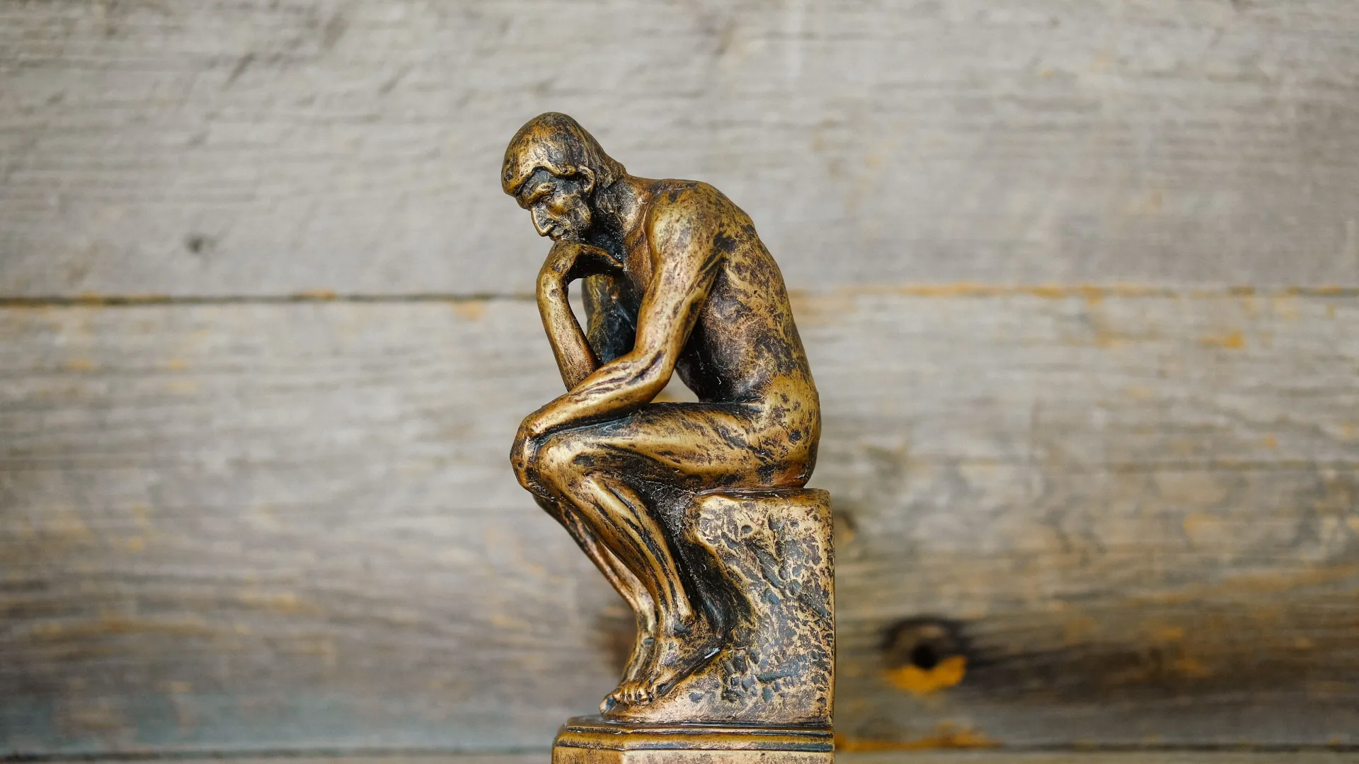 Bronze statue of The Thinker by Rodin depicting a seated man deep in thought on wooden surface.