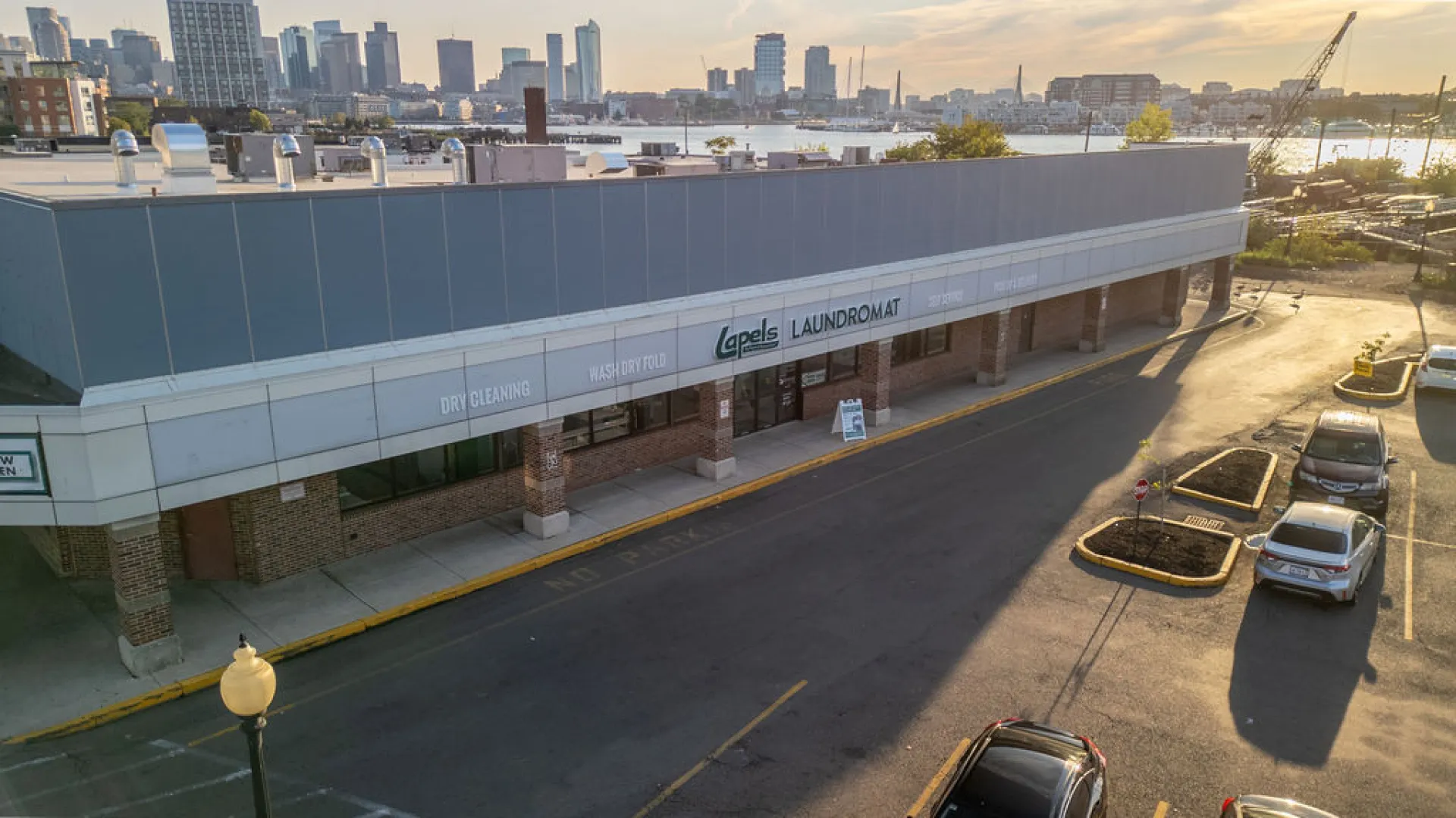 Exterior view of Apels Laundromat and dry cleaning store with city skyline and river in background at sunset