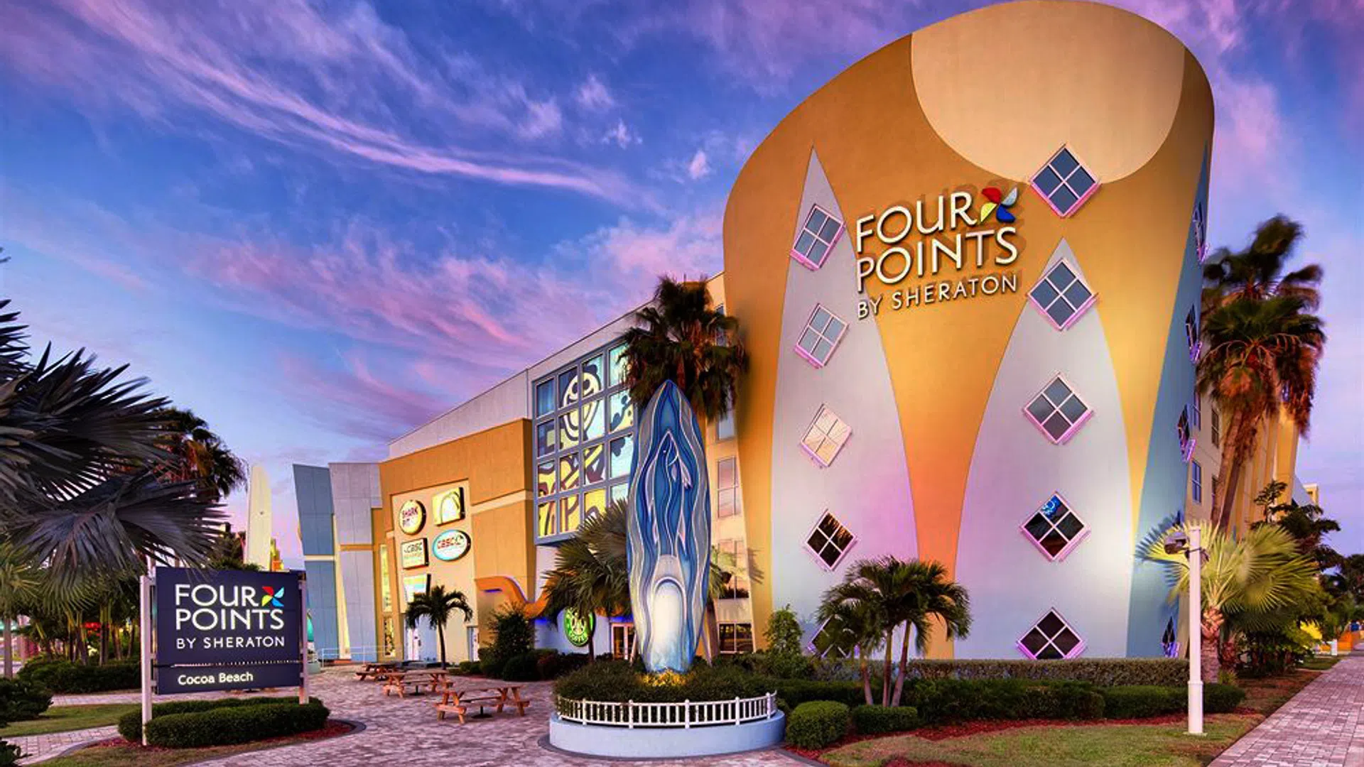 Four Points by Sheraton hotel building with colorful design and palm trees under a vibrant sunset sky.