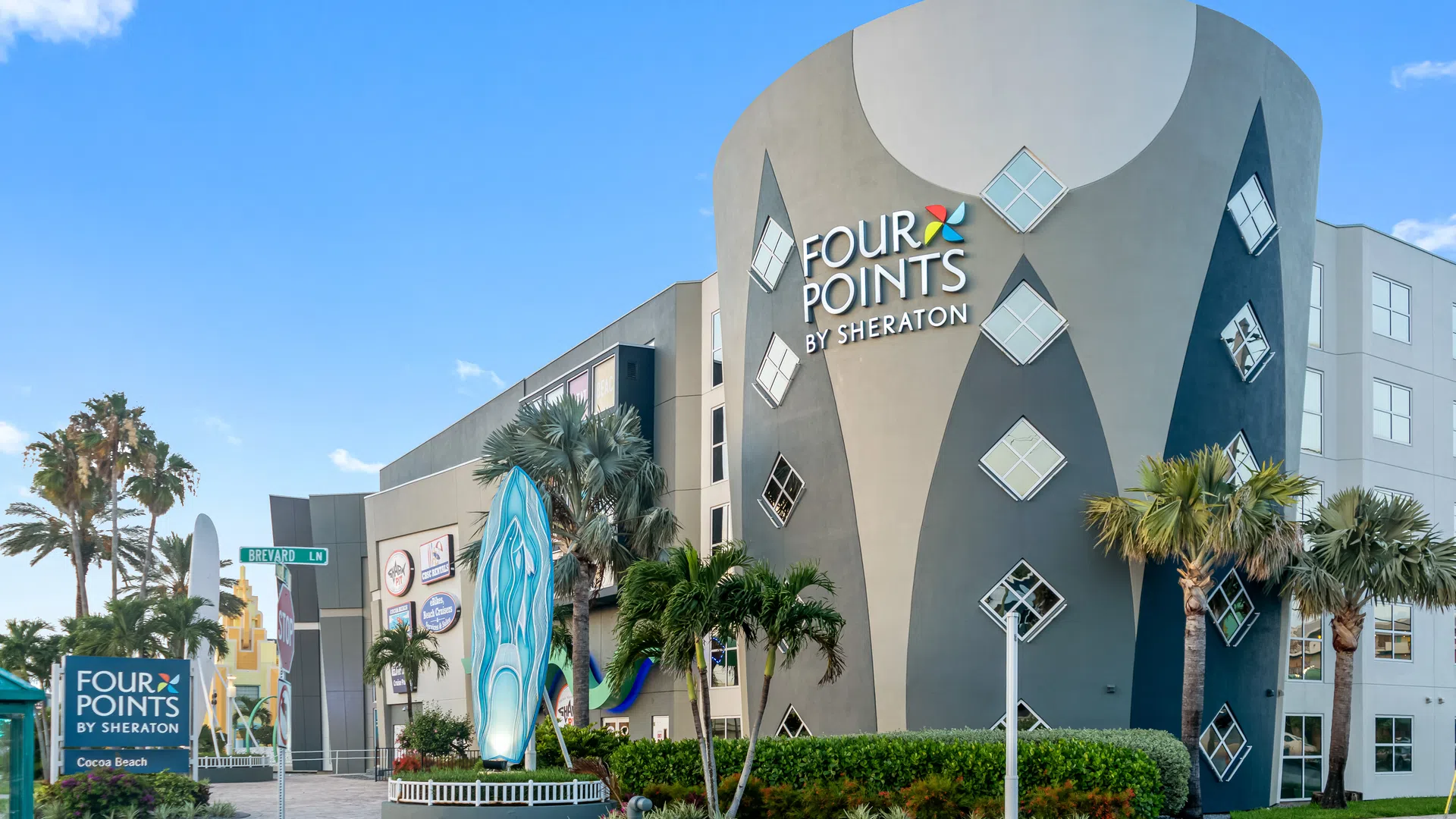 Modern Four Points by Sheraton hotel building with unique curved design and palm trees under a blue sky