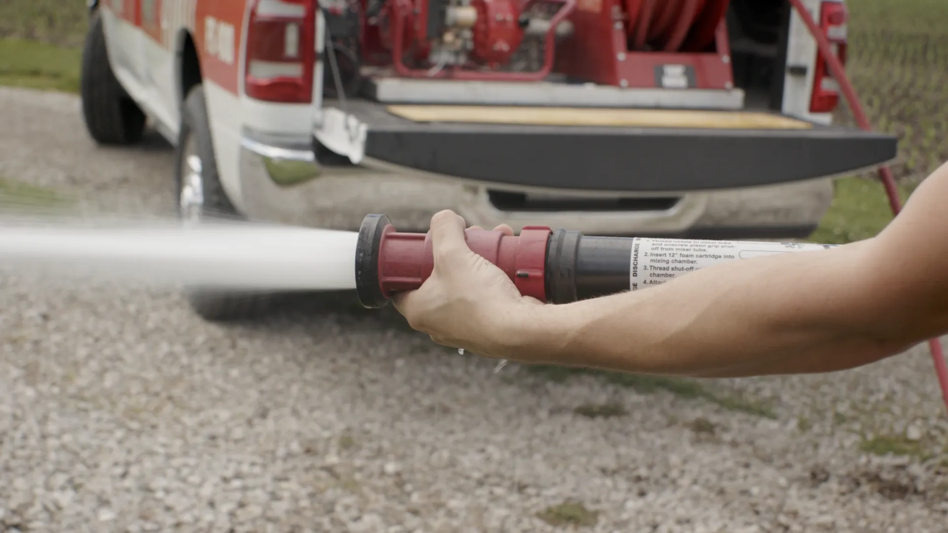 a hand holding a fire suppression hose with a vehicle behind it