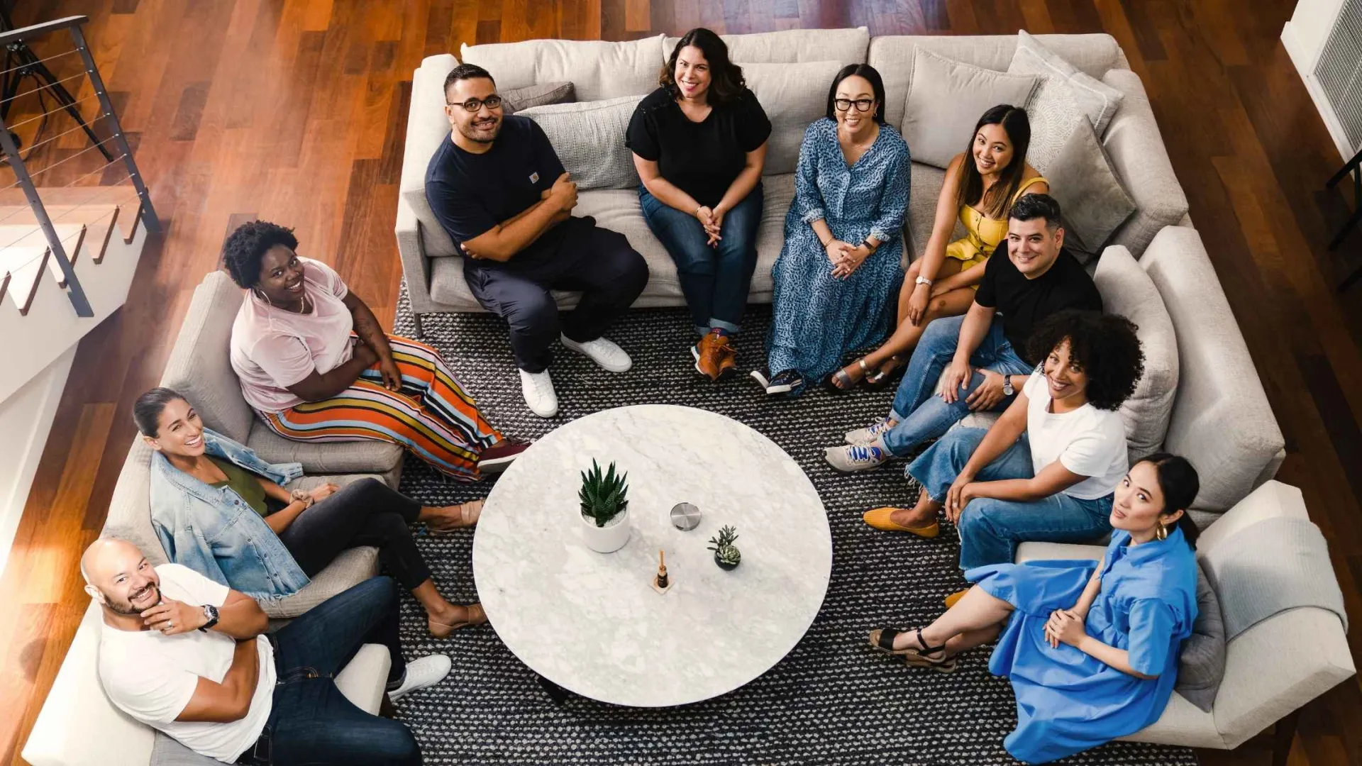 Diverse group of people sitting in a circle on sofas around a round table in a modern living room.