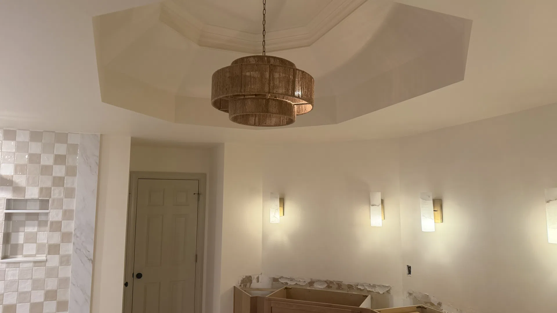 Partially renovated bathroom with wood cabinets, beige walls, mosaic tile shower, and a tiered pendant light fixture