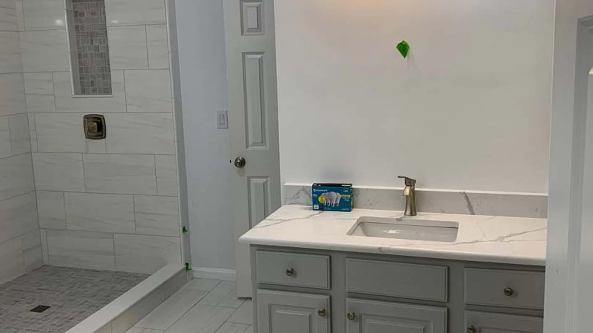 Modern bathroom with gray vanity, white countertop, built-in shower with tiled walls and floor, and overhead lighting.