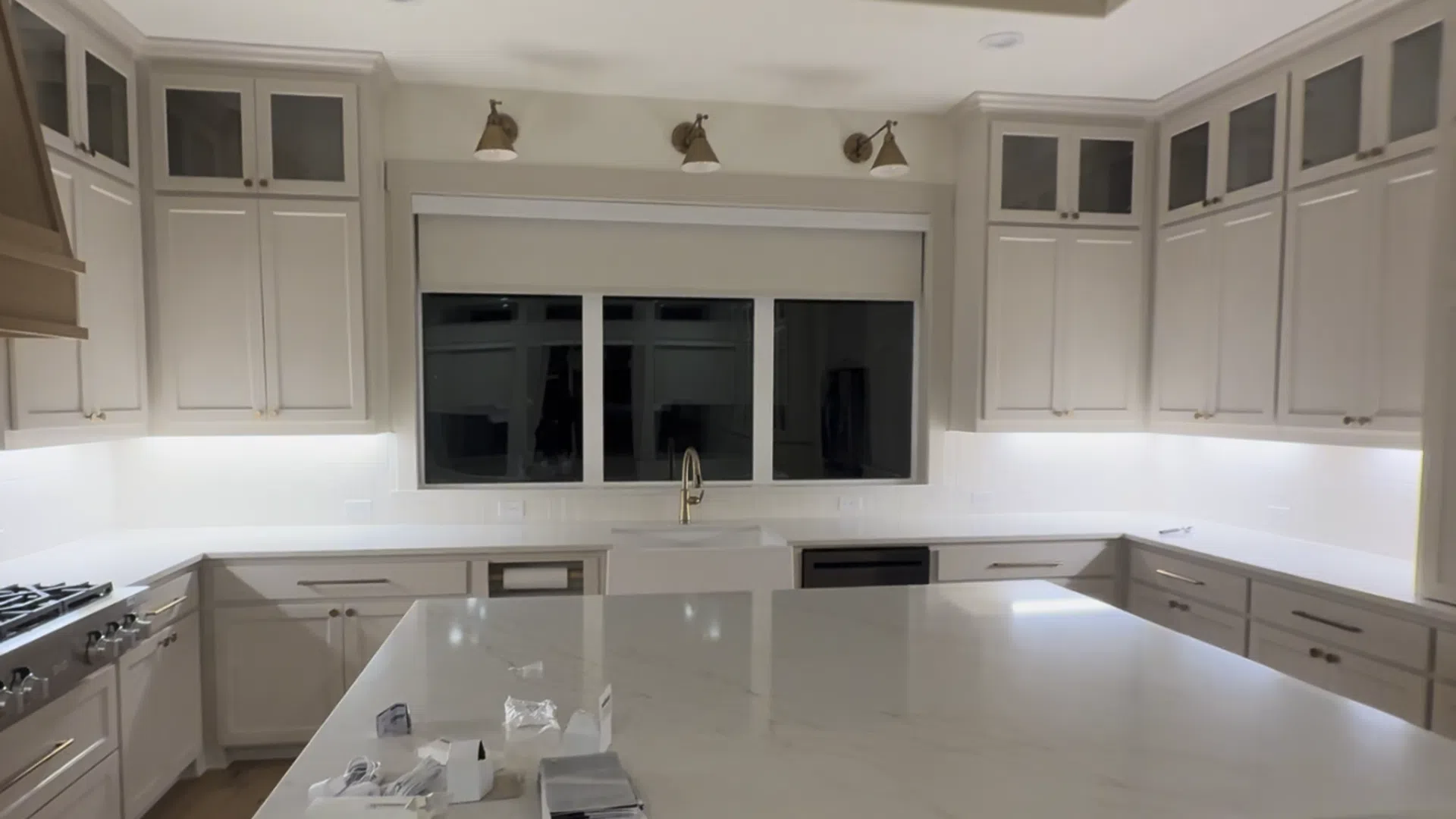 Modern kitchen with white cabinets, large marble island, stainless appliances, and under-cabinet lighting.
