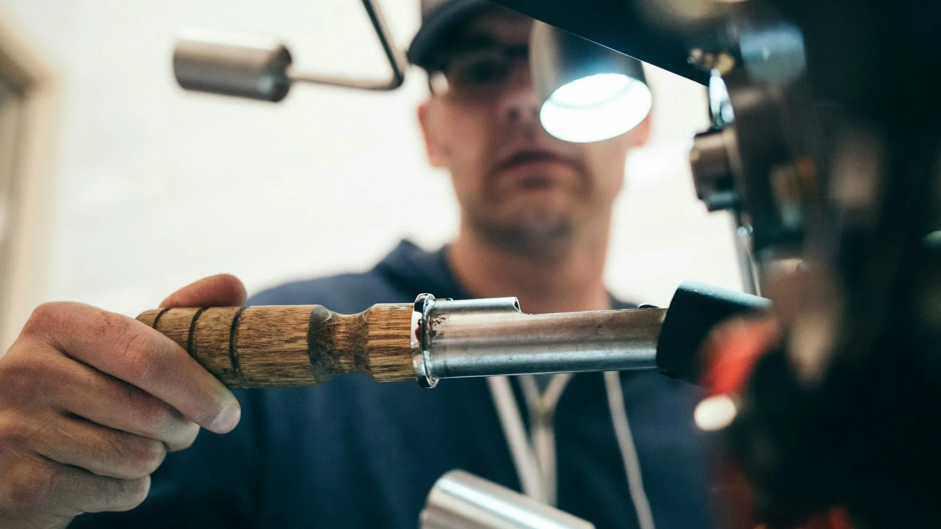Barista using wooden-handled portafilter on espresso machine to prepare coffee shot indoors.