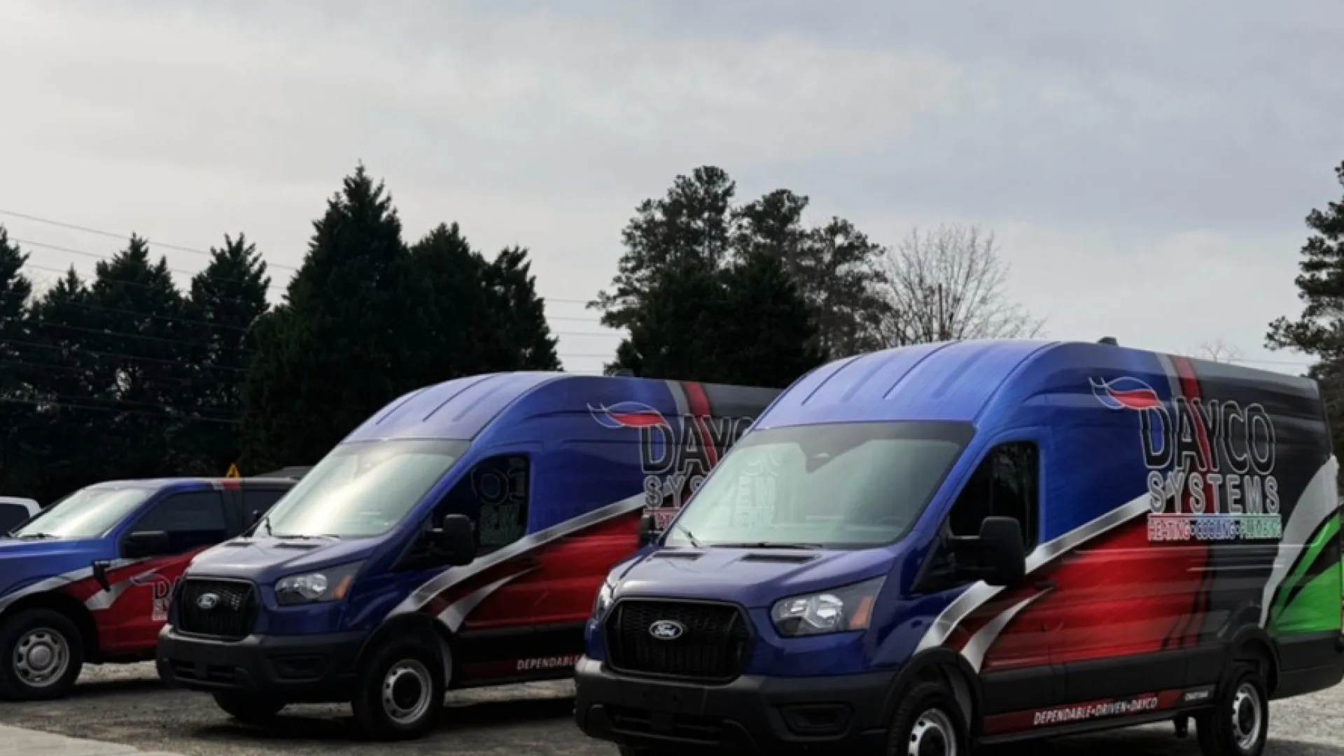 Two blue and red Ford vans with Dayco Systems branding parked outdoors on a cloudy day.