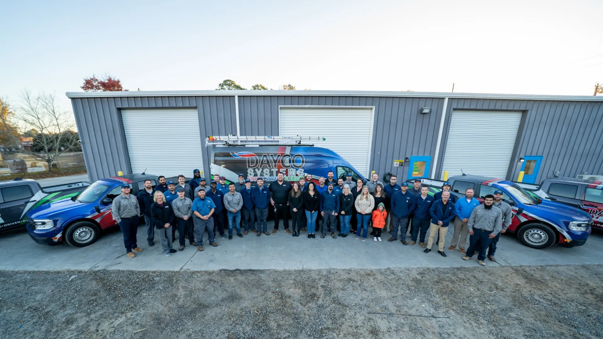 Large group of people standing in front of a building with company vans labeled Dayco Systems and Tracker.