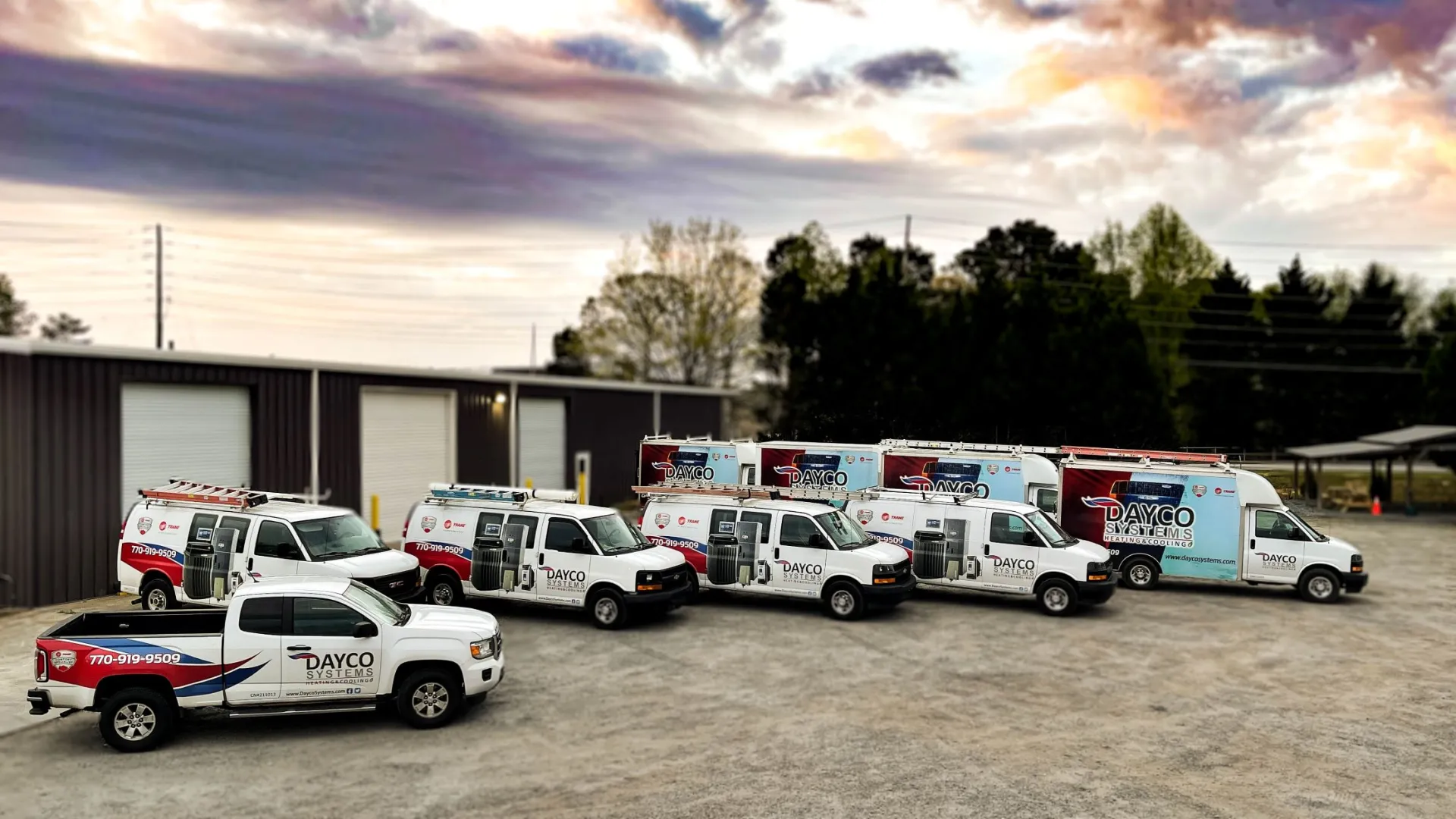 Fleet of Dayco Systems service trucks and vans parked outside a warehouse under a dramatic sky.