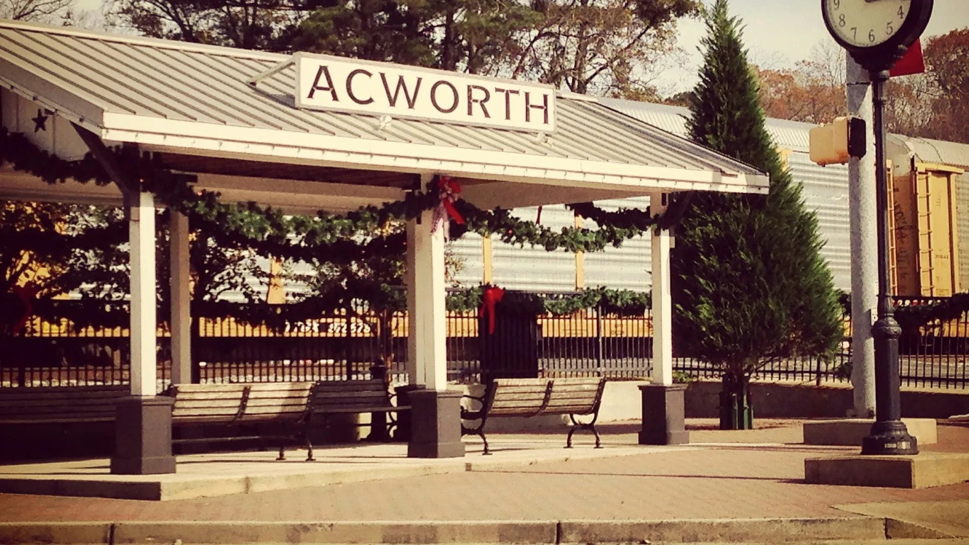 Acworth train station shelter with benches and clock post surrounded by trees and holiday decorations