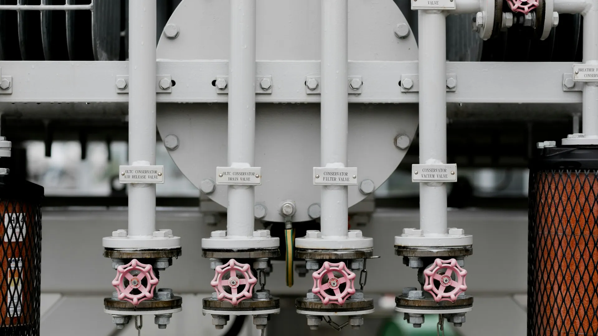 Close-up of industrial white metal pipes with pink valve handles and labeled tags in a factory setting.