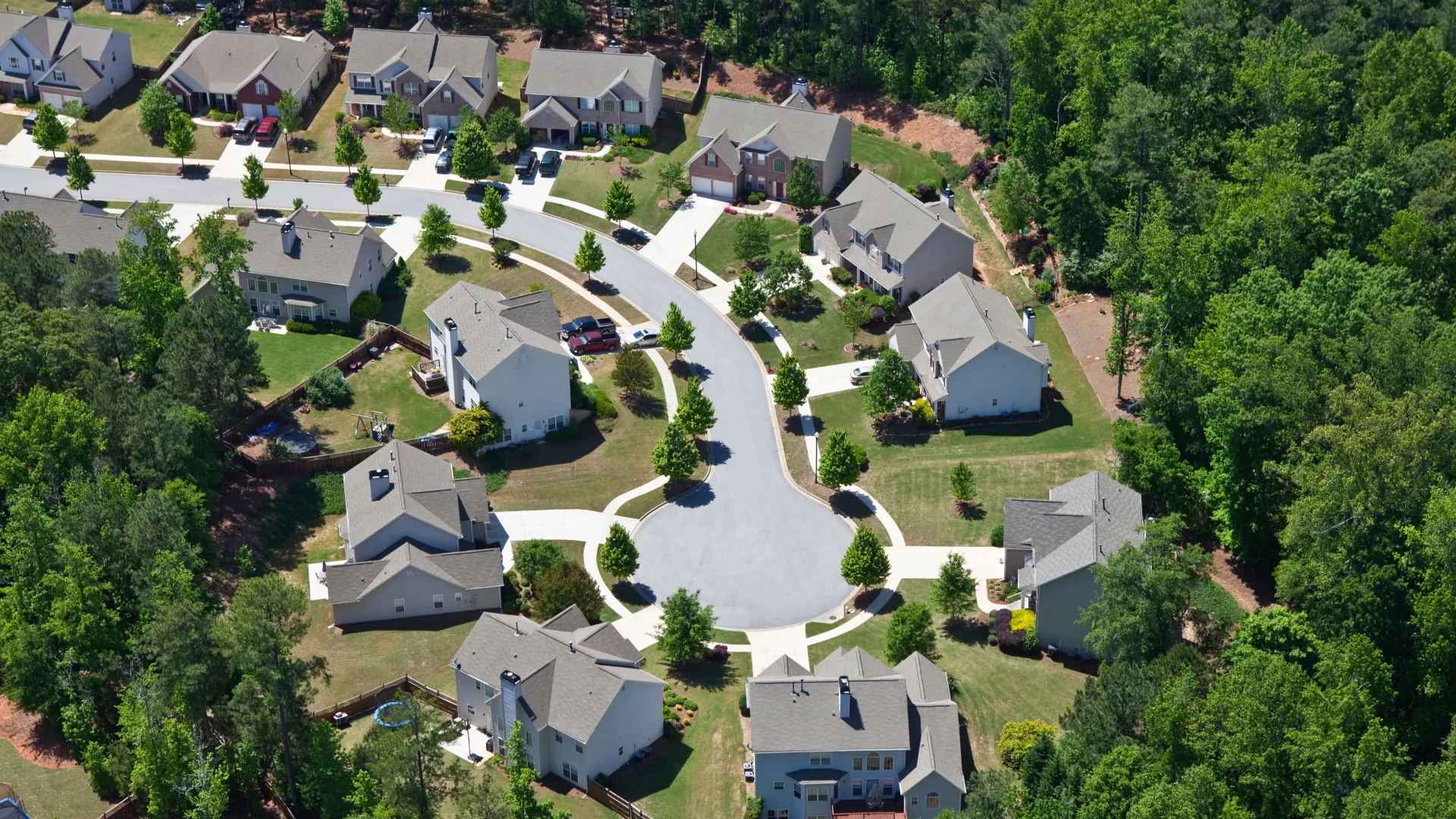 Aerial view of a suburban cul-de-sac with single-family homes surrounded by dense green trees under clear skies