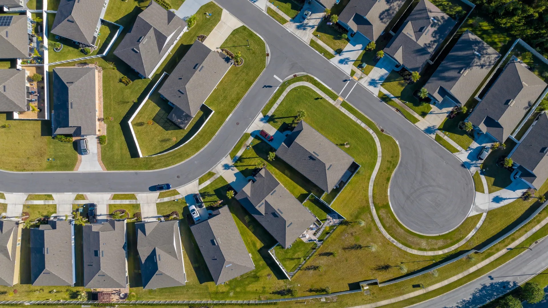Aerial view of a suburban neighborhood with houses, curved streets, and green lawns under daylight.