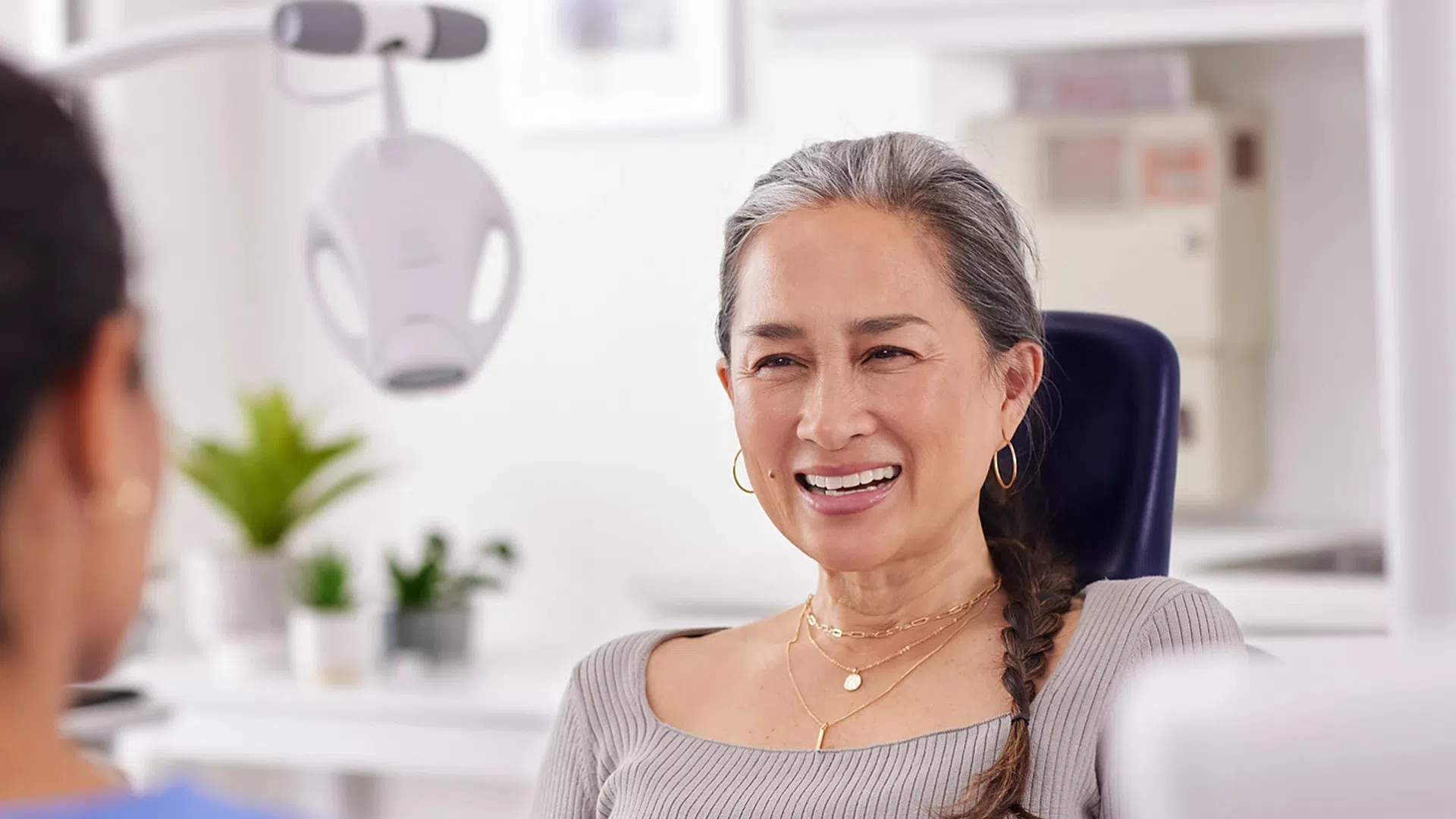 Smiling woman with braided hair in a dental office talking to a healthcare professional.