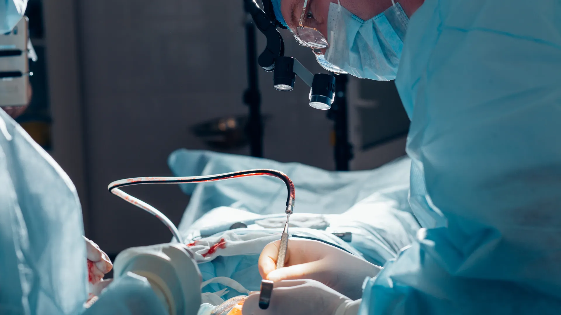 Surgeons in protective gear perform a precise operation in a sterile operating room under bright surgical lights.