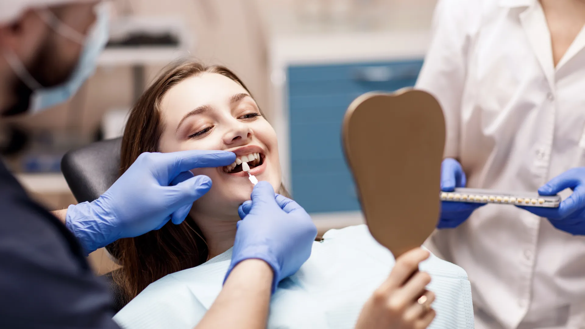 Dentist fitting dental veneers on smiling woman holding hand mirror in dental clinic