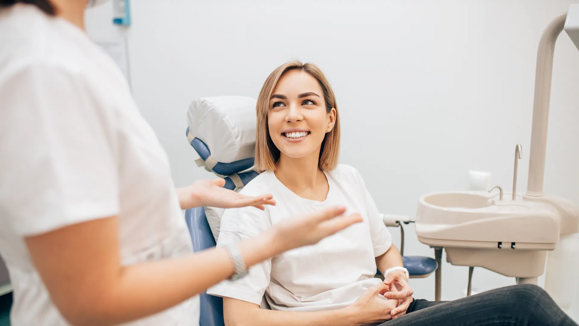 Smiling woman seated in dental chair listening to female dentist explaining treatment in clinic
