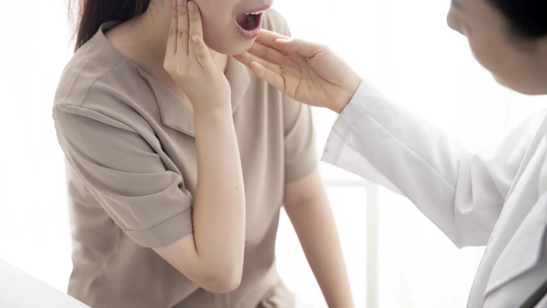 Doctor examining woman's swollen jaw and neck area during medical consultation in bright clinic room