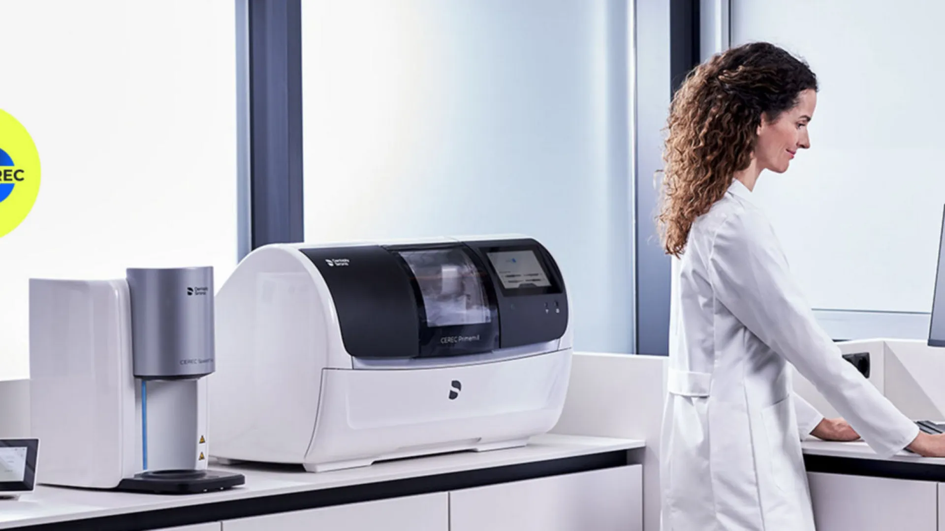 Female dentist uses dental CAD/CAM software with milling machine and scanner in a bright modern clinic.