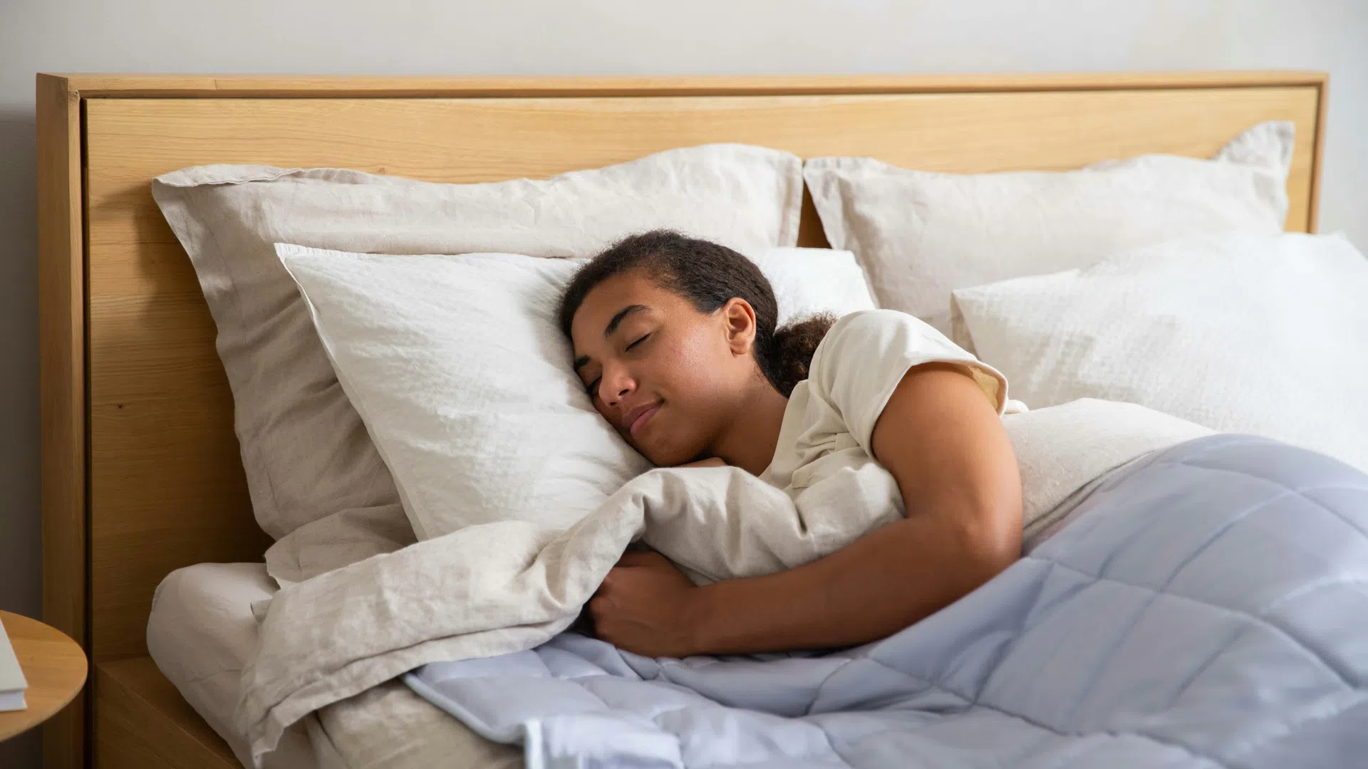 Peaceful woman sleeping comfortably in a cozy bed with white and blue bedding in a wooden headboard bedroom.