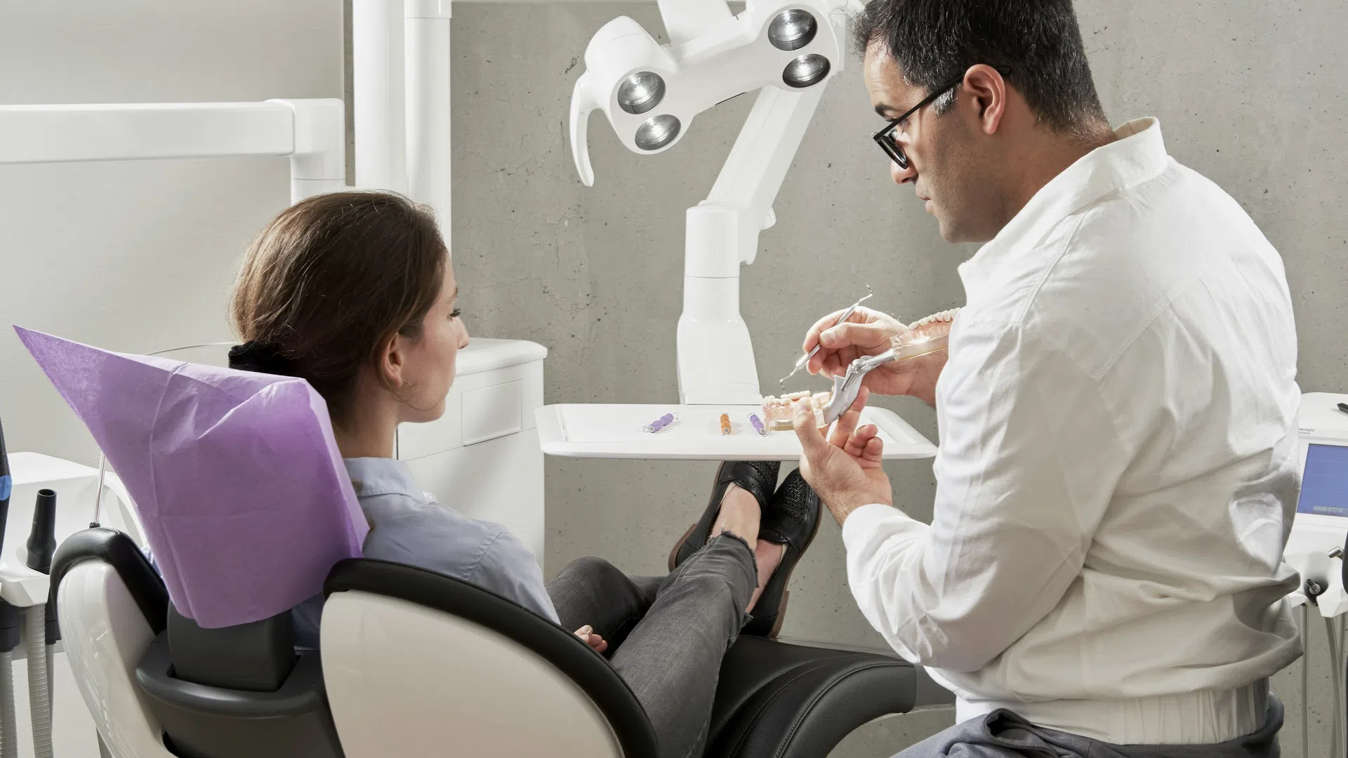 Dentist explains dental implant procedure to patient seated in dental chair with equipment in background
