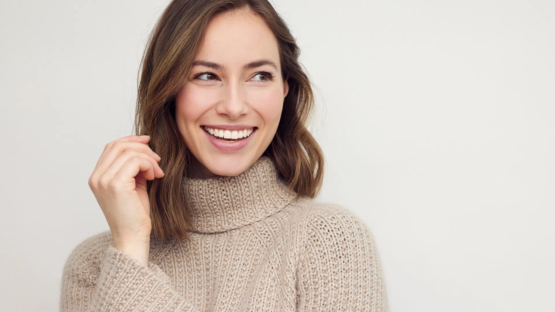 Smiling woman wearing a beige knitted turtleneck sweater against a plain light background