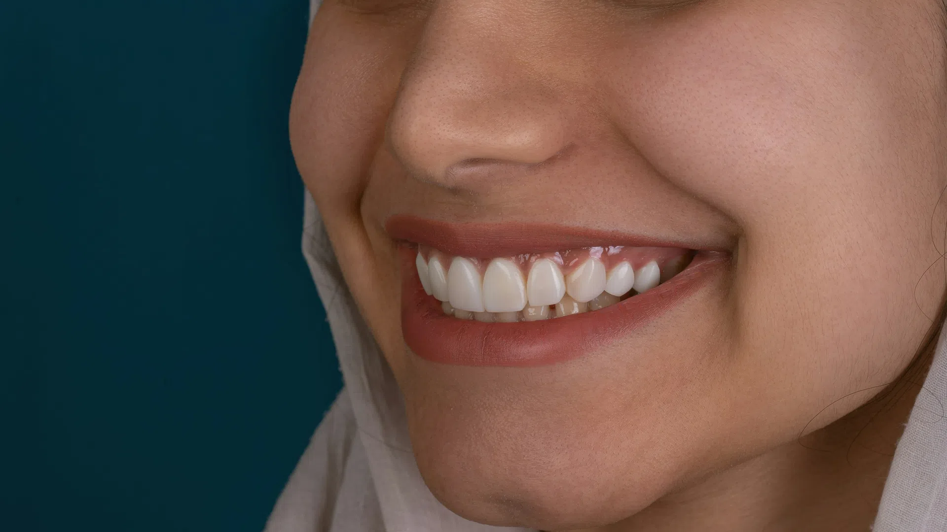 Close-up of a smiling woman with perfect white teeth and natural skin against a dark blue background.