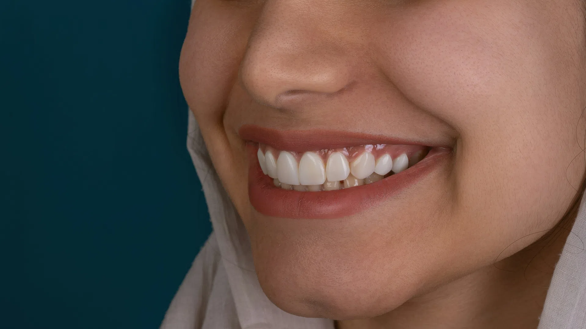 Close-up of a smiling woman with perfect white teeth and natural skin against a dark blue background.