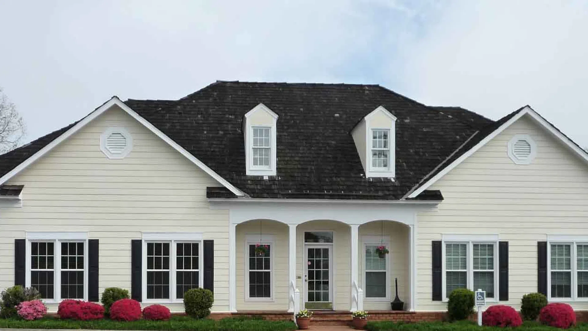 White single-story house with black shutters, dormer windows, brick chimney, and landscaped front yard.