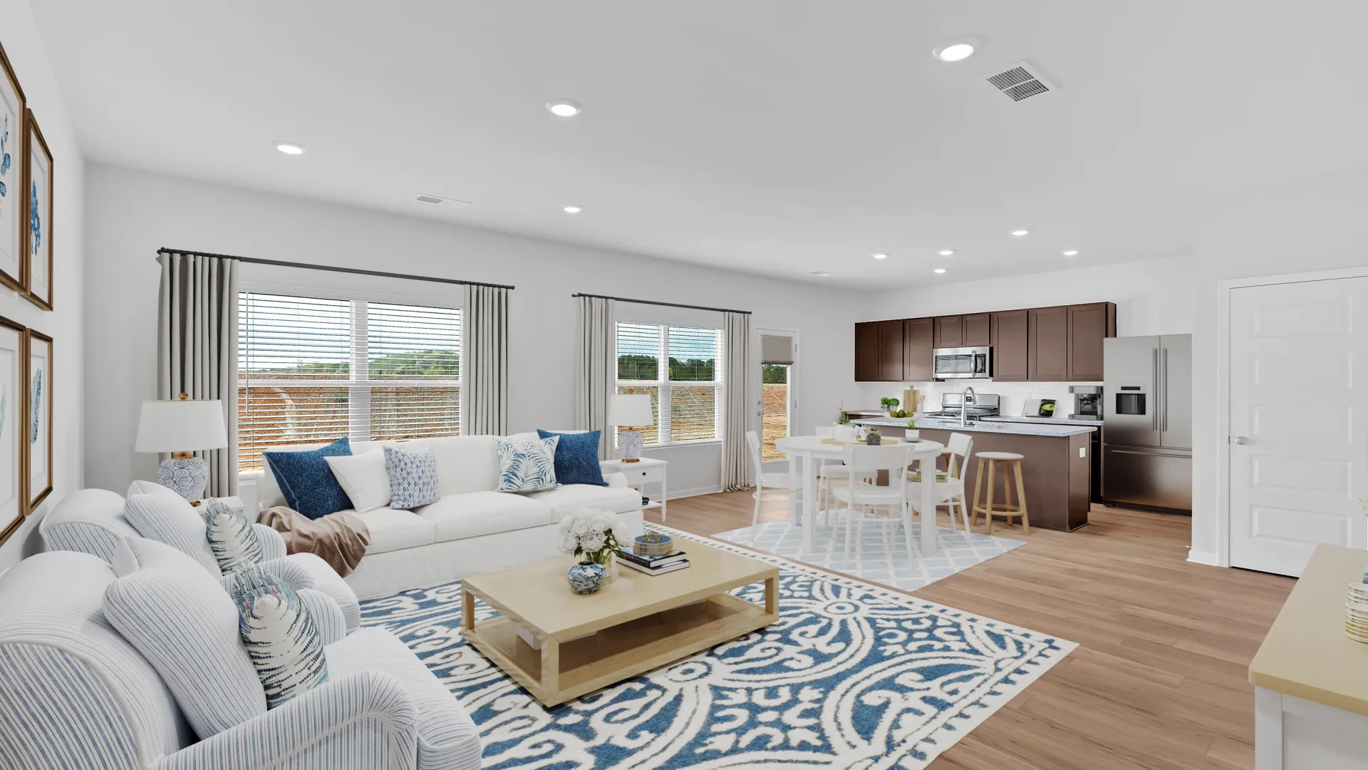 Open-concept living room and kitchen with white walls, blue patterned rugs, and modern furniture in natural light.