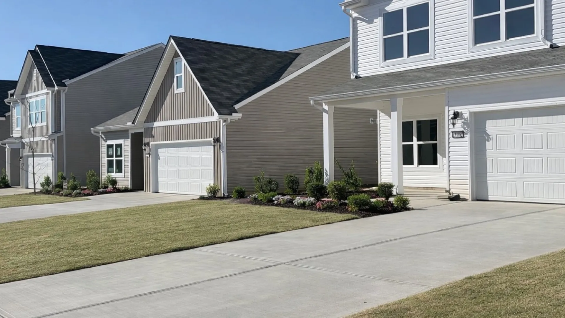 Row of modern suburban houses with well-maintained lawns and clear blue sky on a sunny day.