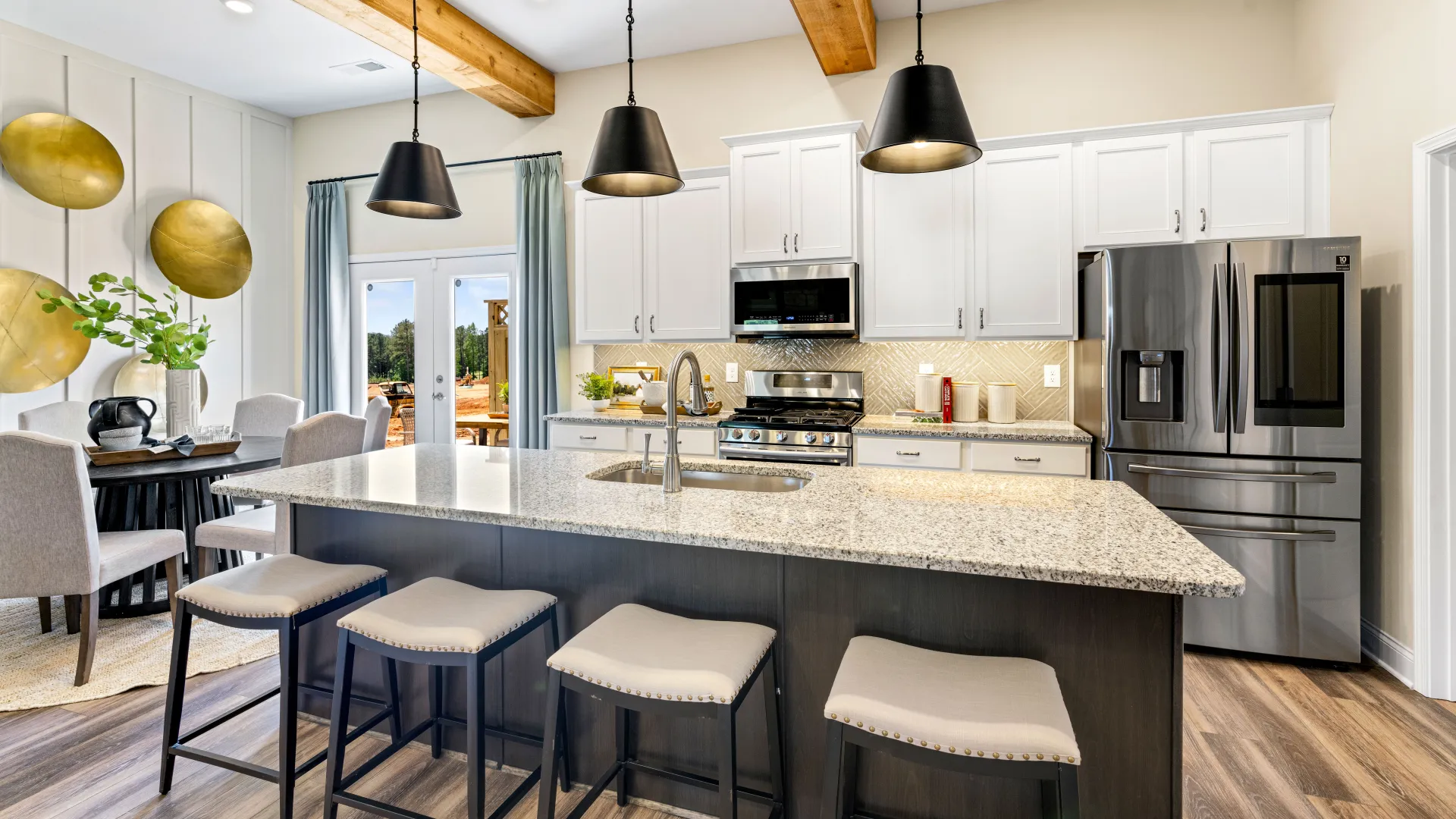 Modern kitchen with granite island, black pendant lights, stainless steel appliances, wooden beams, and dining area.