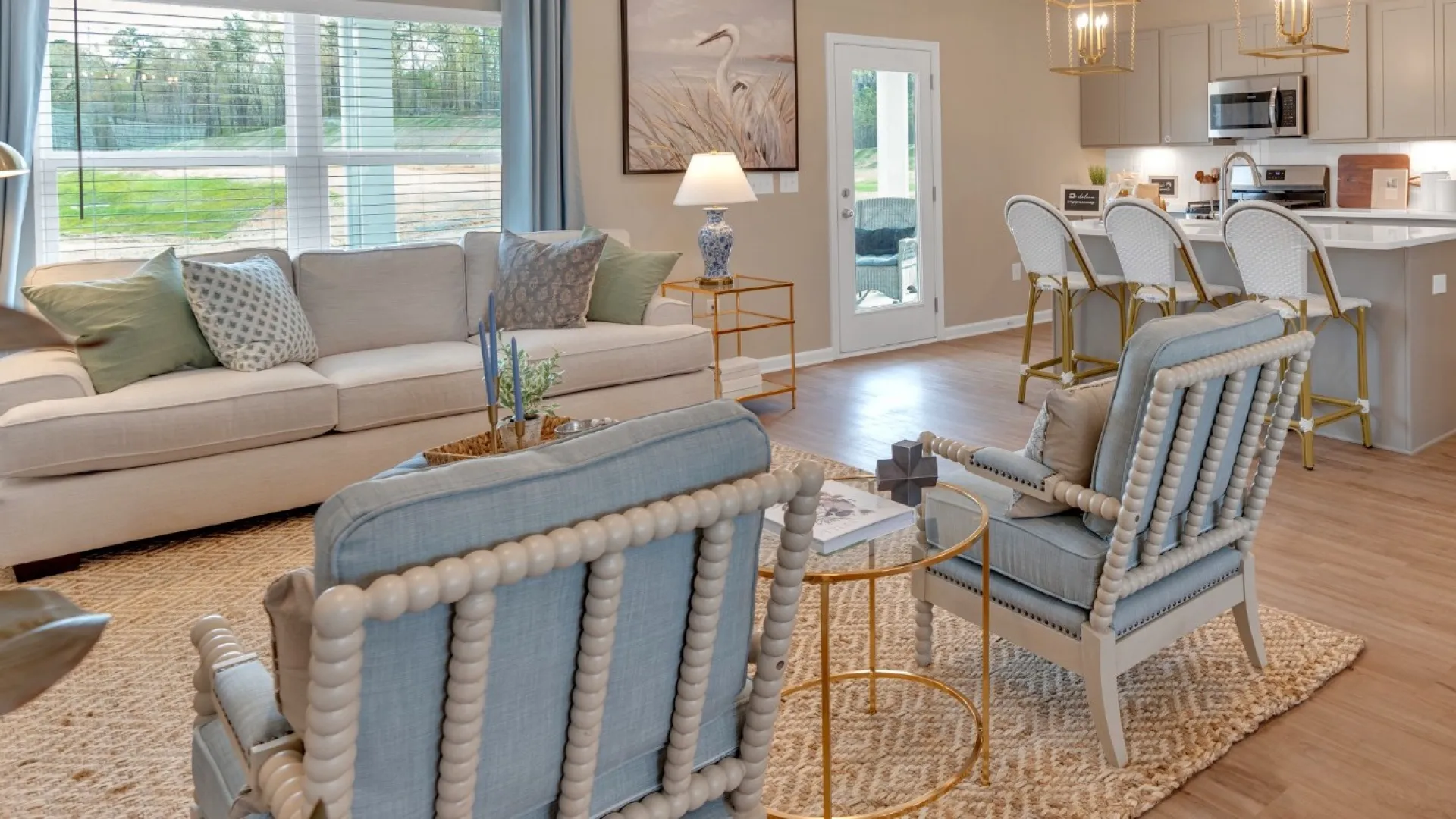 Open living space with beige walls, light wood flooring, blue cushioned chairs, white sofa, and modern kitchen island.