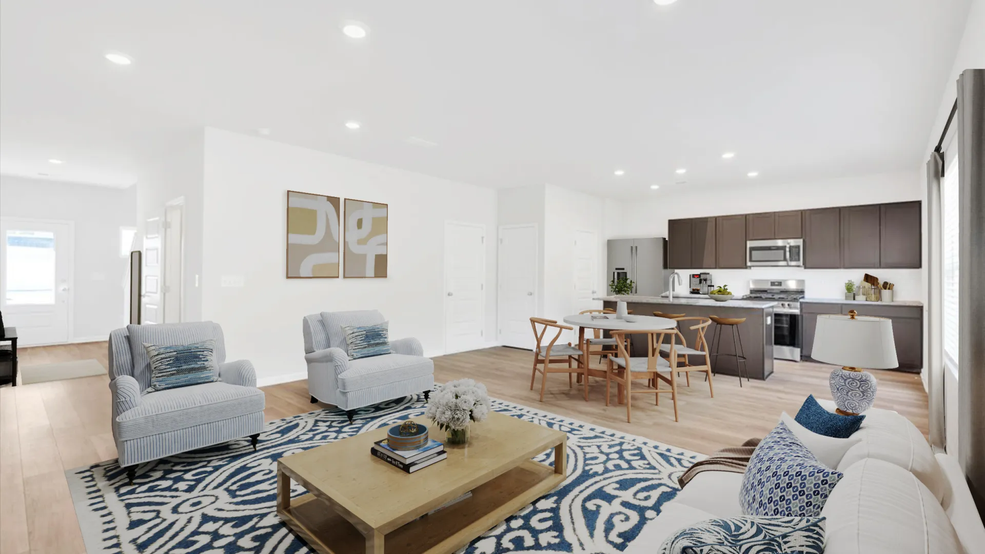 Bright open living room with blue patterned rug, wooden coffee table, armchairs, white sofa, and adjacent kitchen.