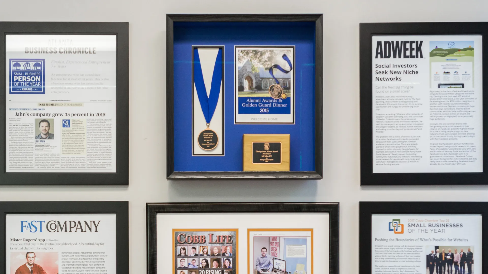 Wall display of framed awards, medals, and notable magazine and newspaper articles about business and innovation.
