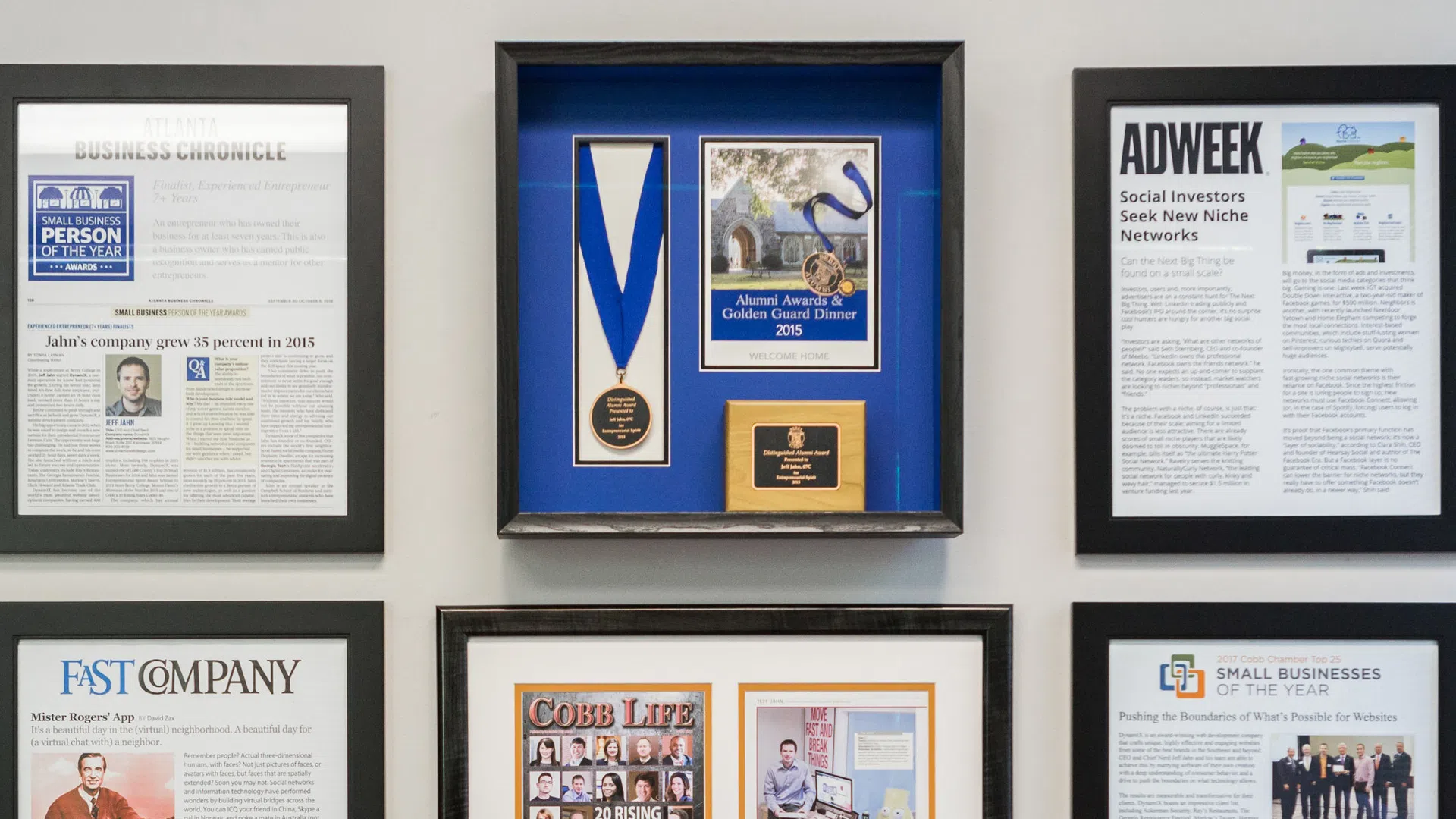 Wall display of framed awards and press articles featuring business and media recognition.