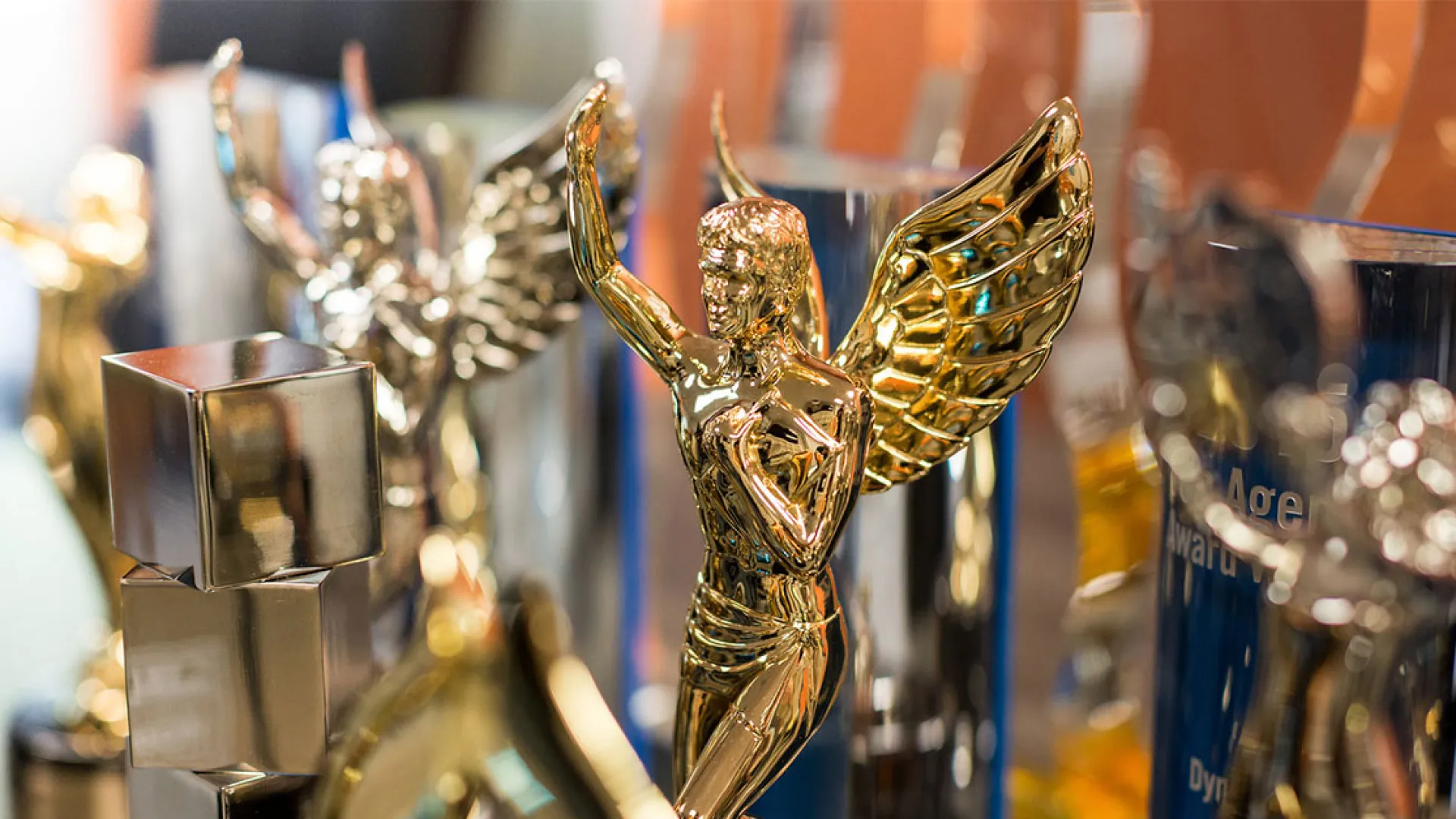 Close-up of shiny gold wings trophy amidst other awards on a display shelf in soft focus background