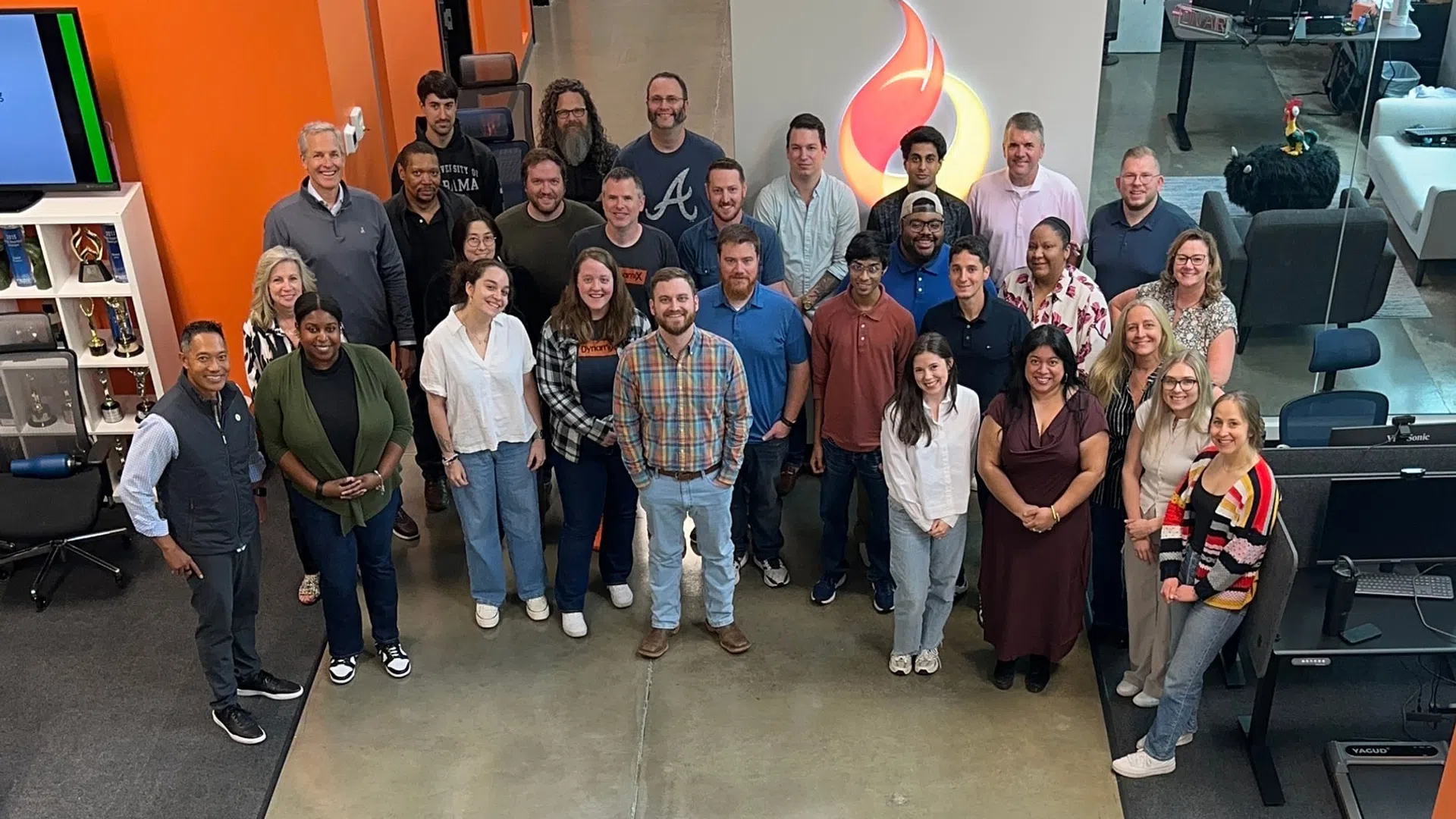Diverse group of coworkers posing in modern office space with concrete floor and flame logo in background