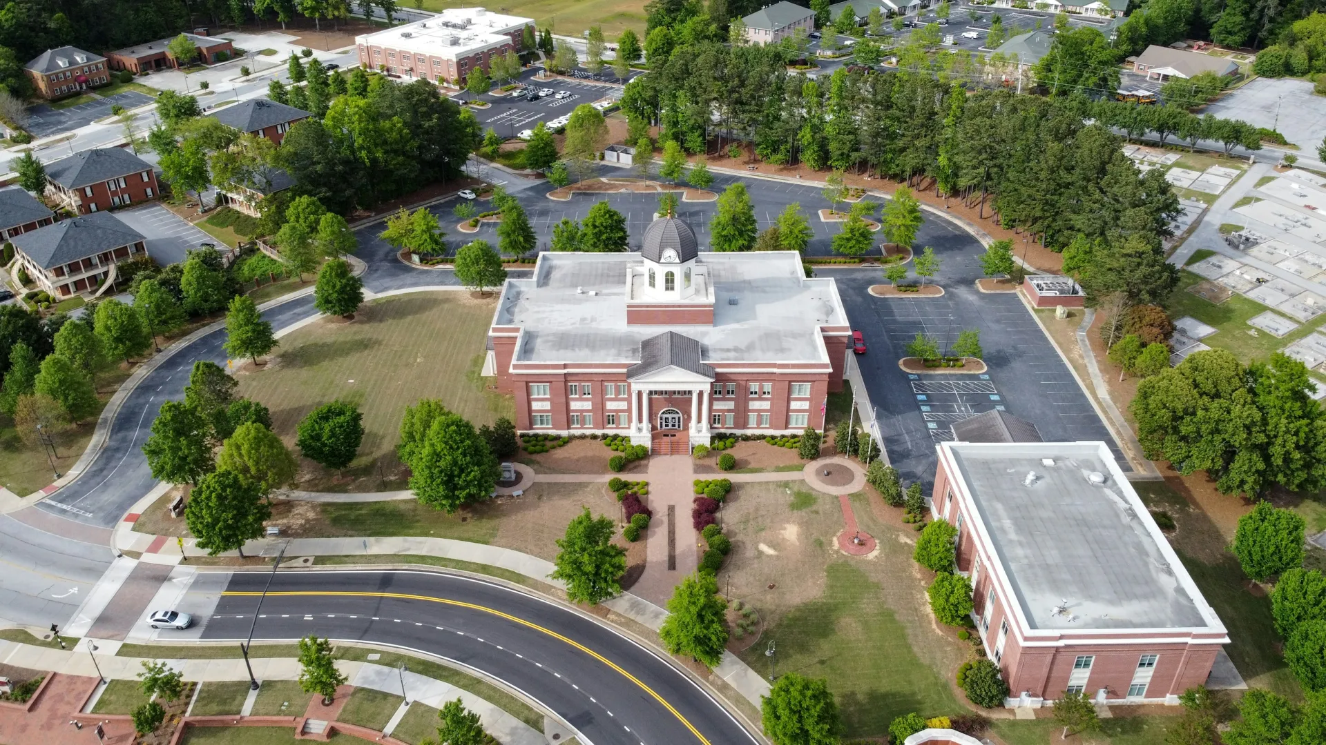 Aerial view of a classic brick courthouse with a white dome surrounded by trees and parking lots on a sunny day