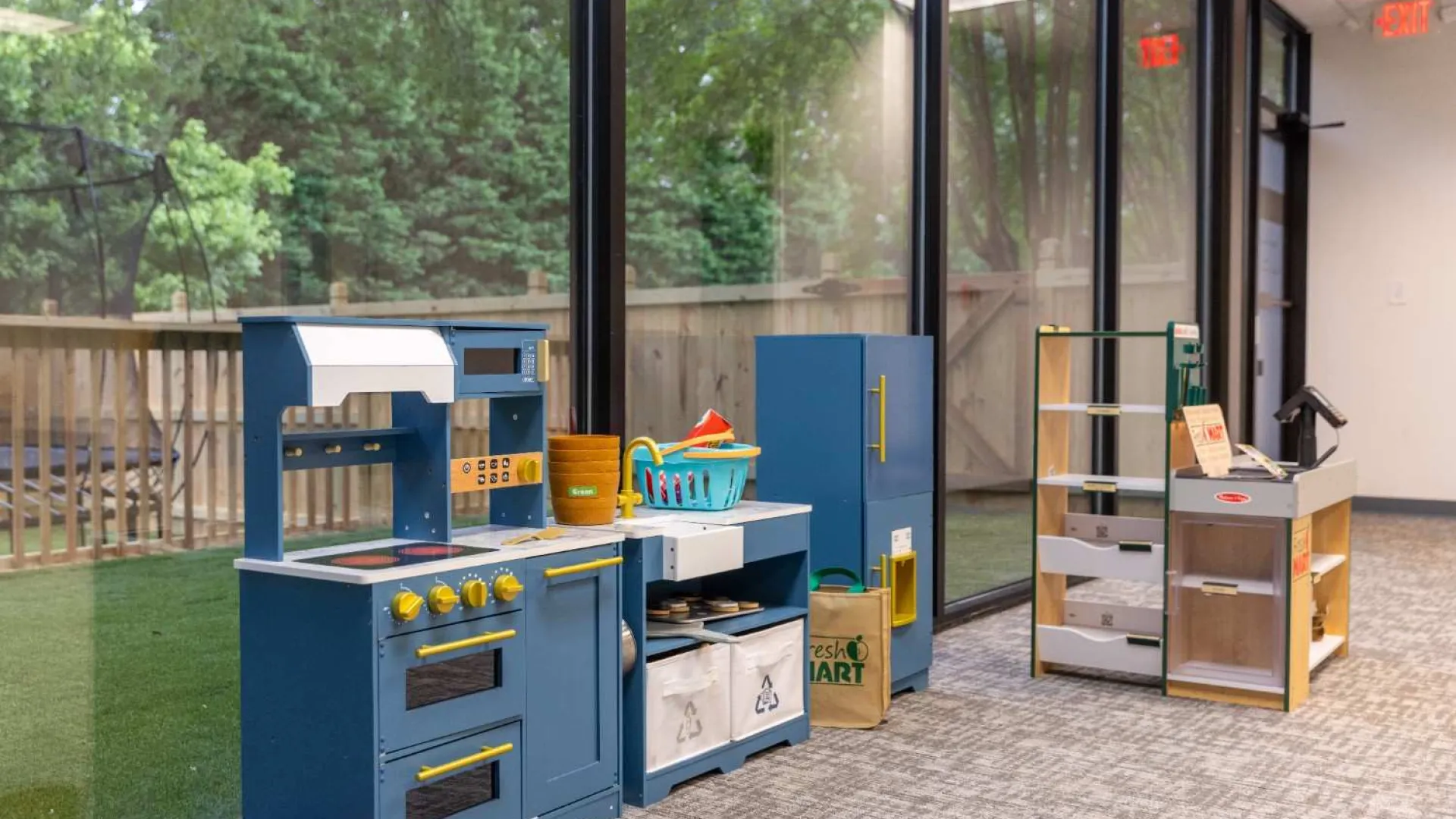 Children's play kitchen and store setup with blue and wood furniture in a bright indoor space beside large windows.