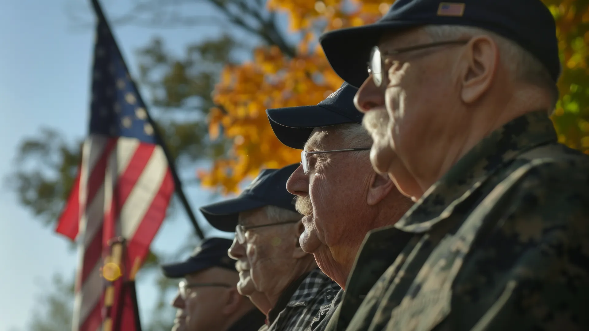 Veterans in caps stand solemnly during a ceremony with an American flag in the background.