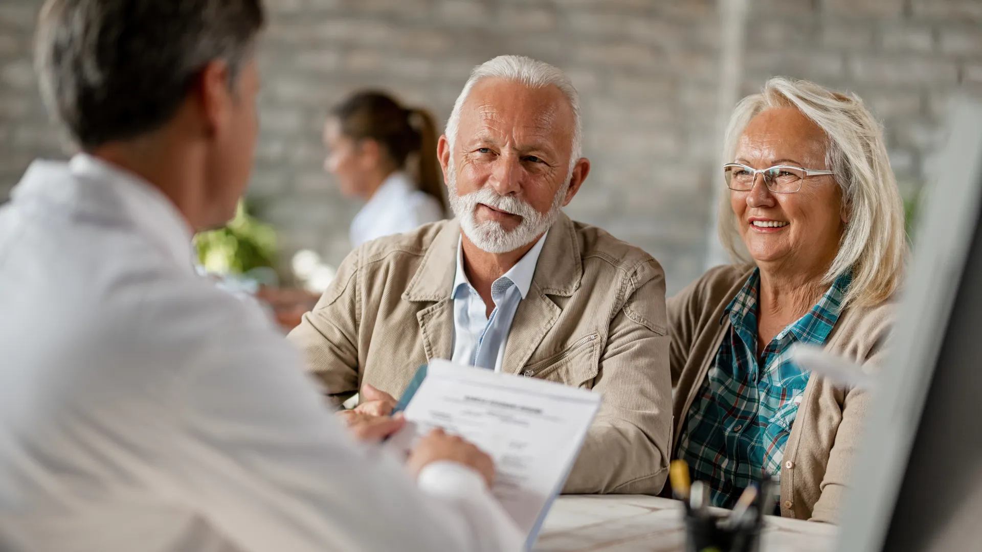 Senior couple consulting a professional man in an office setting, discussing documents and smiling.