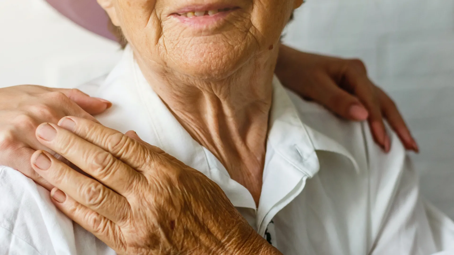 Caregiver gently placing hands on elderly person's shoulder showing support and compassion.