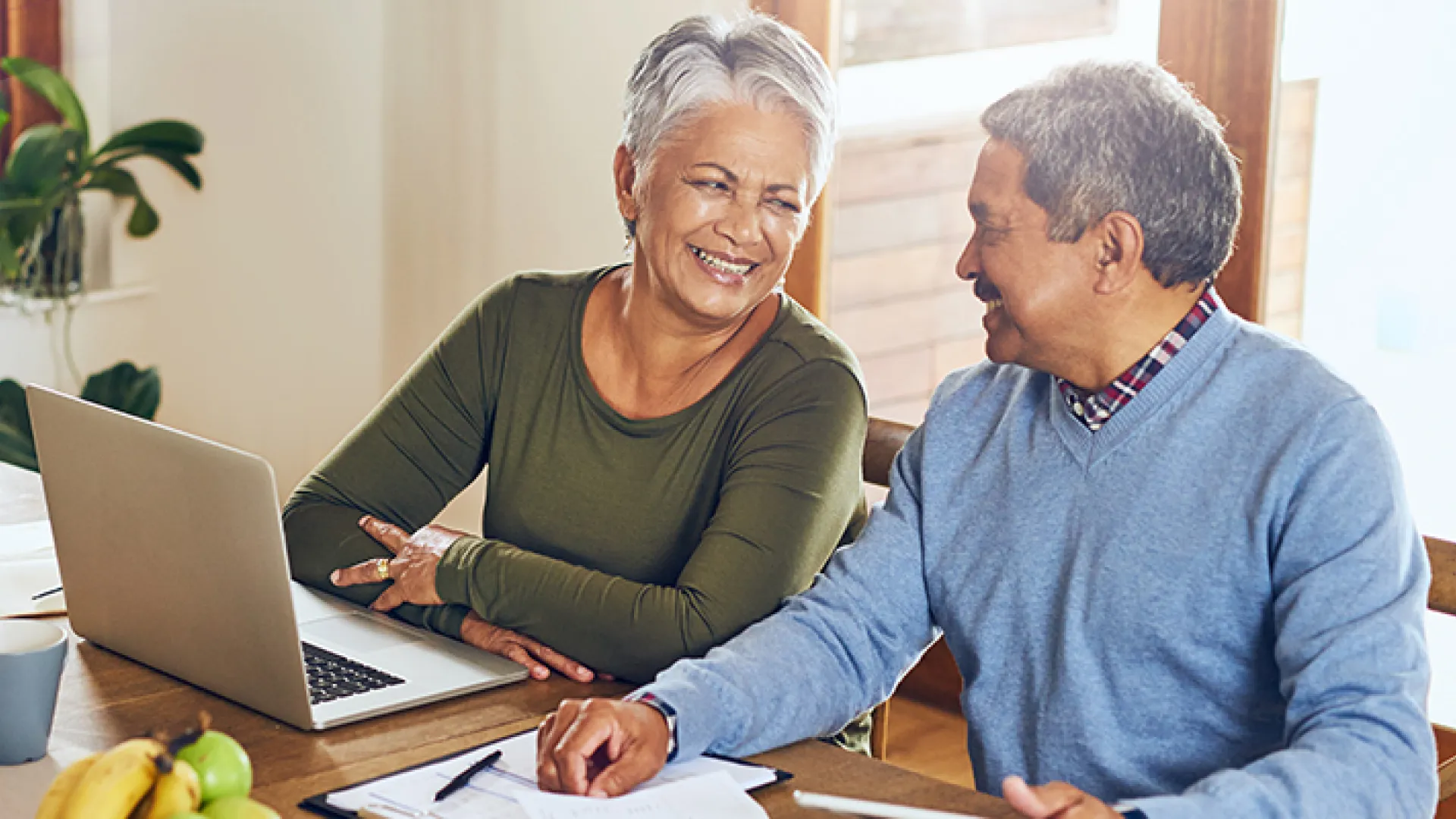 Mature couple planning finances together at kitchen table with laptop and coffee in bright home